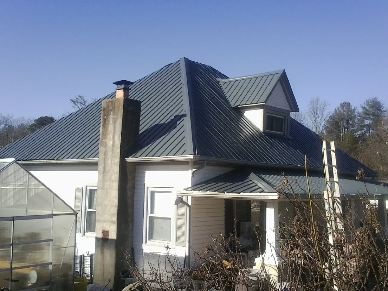 Dark blue standing seam metal roof on a white farmhouse with dormer — Slate & Tile Roof Repair by Roofing Brothers in Buckingham