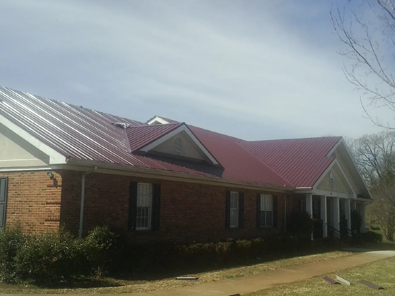 Red metal roof with gabled entries on a long brick building, from a Hail Damage Roof Repair job in Buckingham