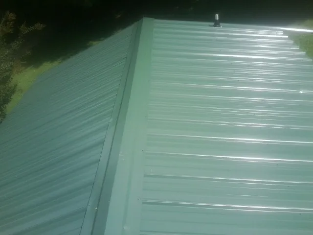 New green metal panels meeting at the ridge of a roof — Flat Roof Repair work by our crew in Buckingham